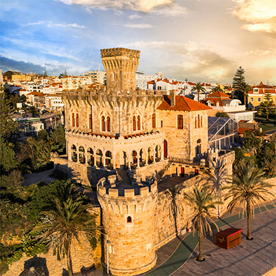 Castle-style stone building with turrets and palm trees at sunset in Estoril, Portugal